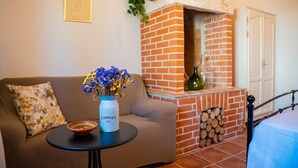 Ein Wohnzimmer mit Kamin aus Ziegelsteinen, einer Couch, einem kleinen Tisch mit Schale und Blumenvase, und einer Tür im Hintergrund.
