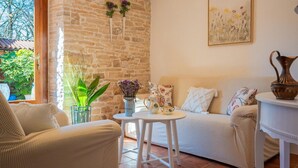 Ein gemütliches Wohnzimmer mit Steinwand, einer Couch, einem kleinen runden Tisch und einer Vase mit Blumen.