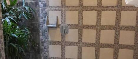 A bathroom with a shower, tiled walls, a toilet, and a plant.