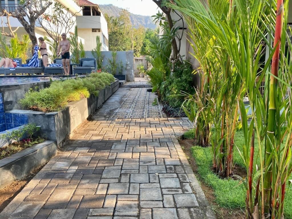 Un camino pavimentado que conduce a una zona de piscina con sillas de descanso y una persona tomando el sol.