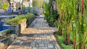 Un camino pavimentado que conduce a una zona de piscina con sillas de descanso y una persona tomando el sol.