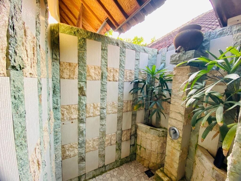 A small, enclosed outdoor shower area with a tiled floor and a stone wall.