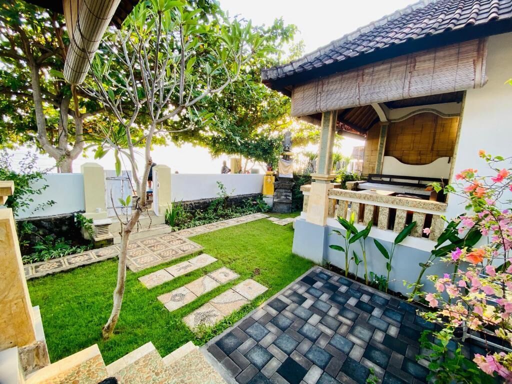 Un bâtiment de style traditionnel, doté d’un toit en tuiles, d’un petit jardin avec une pelouse et des pas japonais, et d’une clôture décorative.