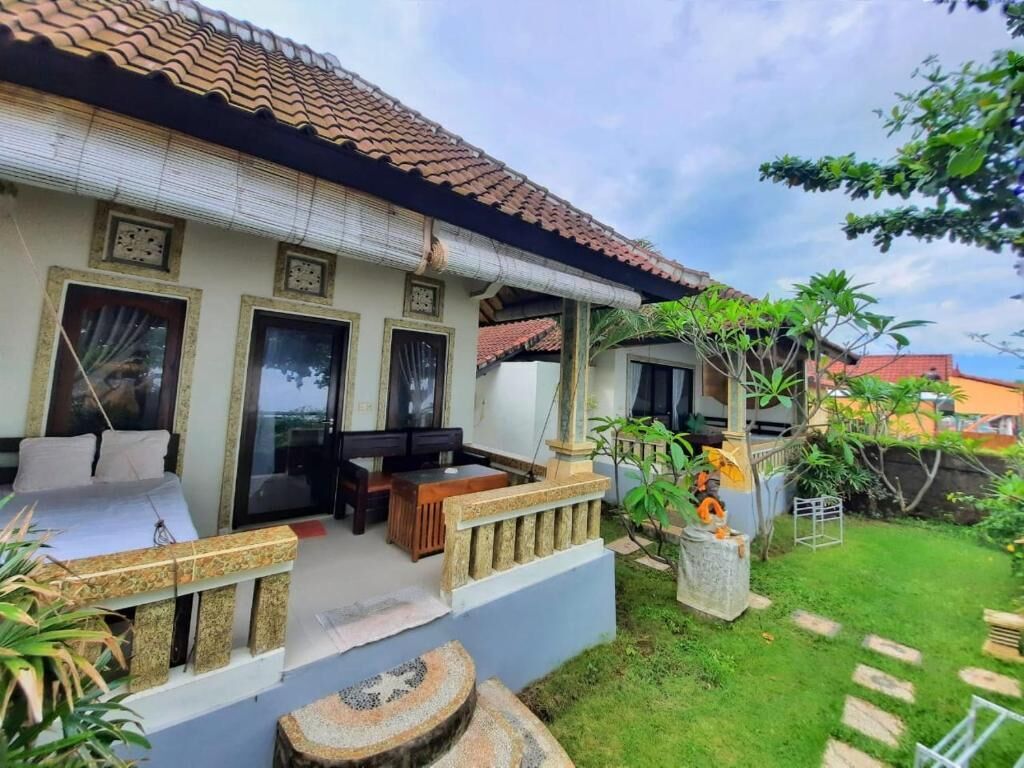 A traditional house with a tiled roof, a balcony with a sofa and table, and a small garden with a tree and a decorative stone.