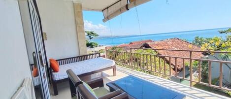A balcony with a view of the sea, a sofa, a table, and a bed.