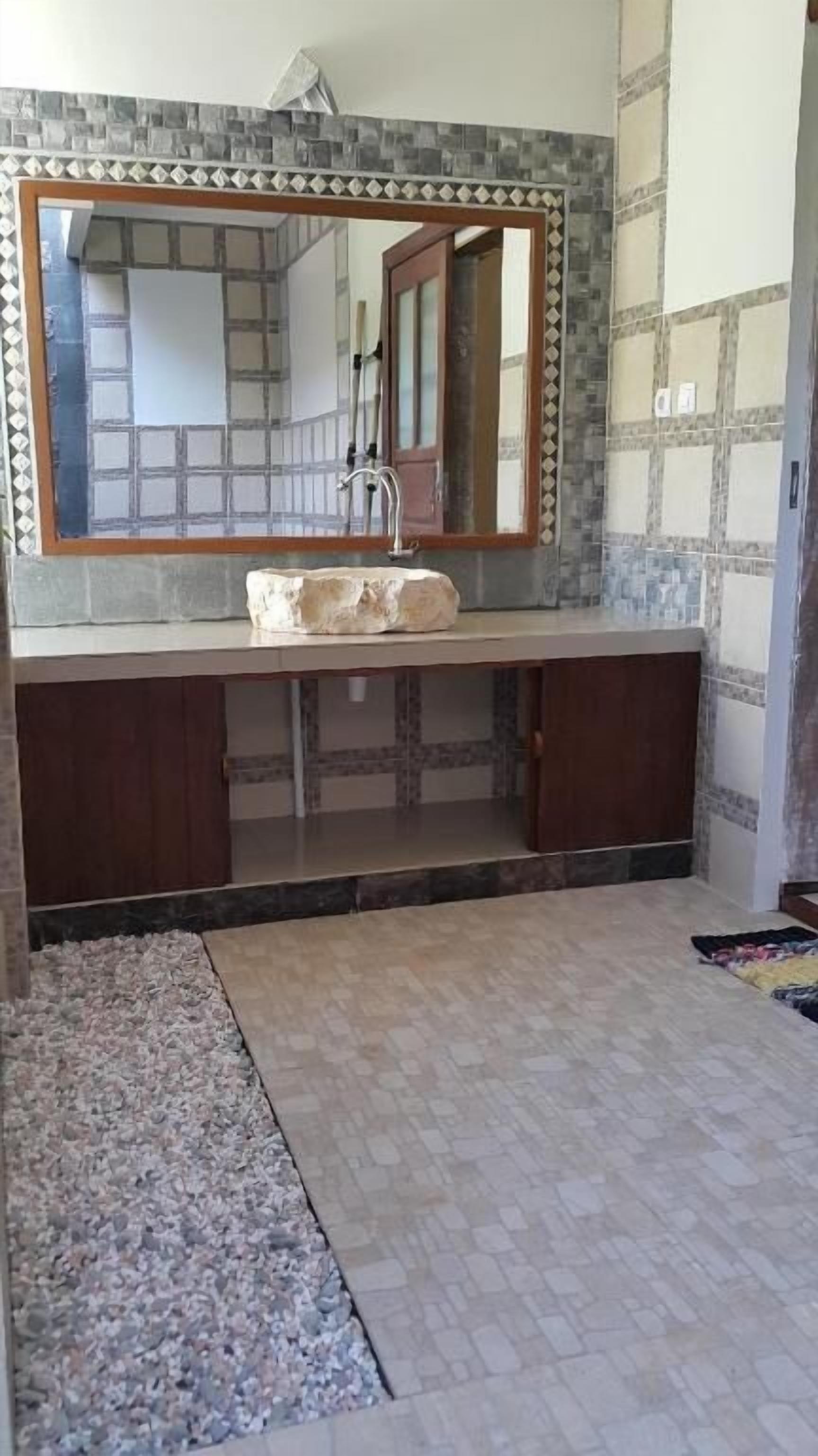A bathroom with a stone sink, a large mirror, and a tiled backsplash.
