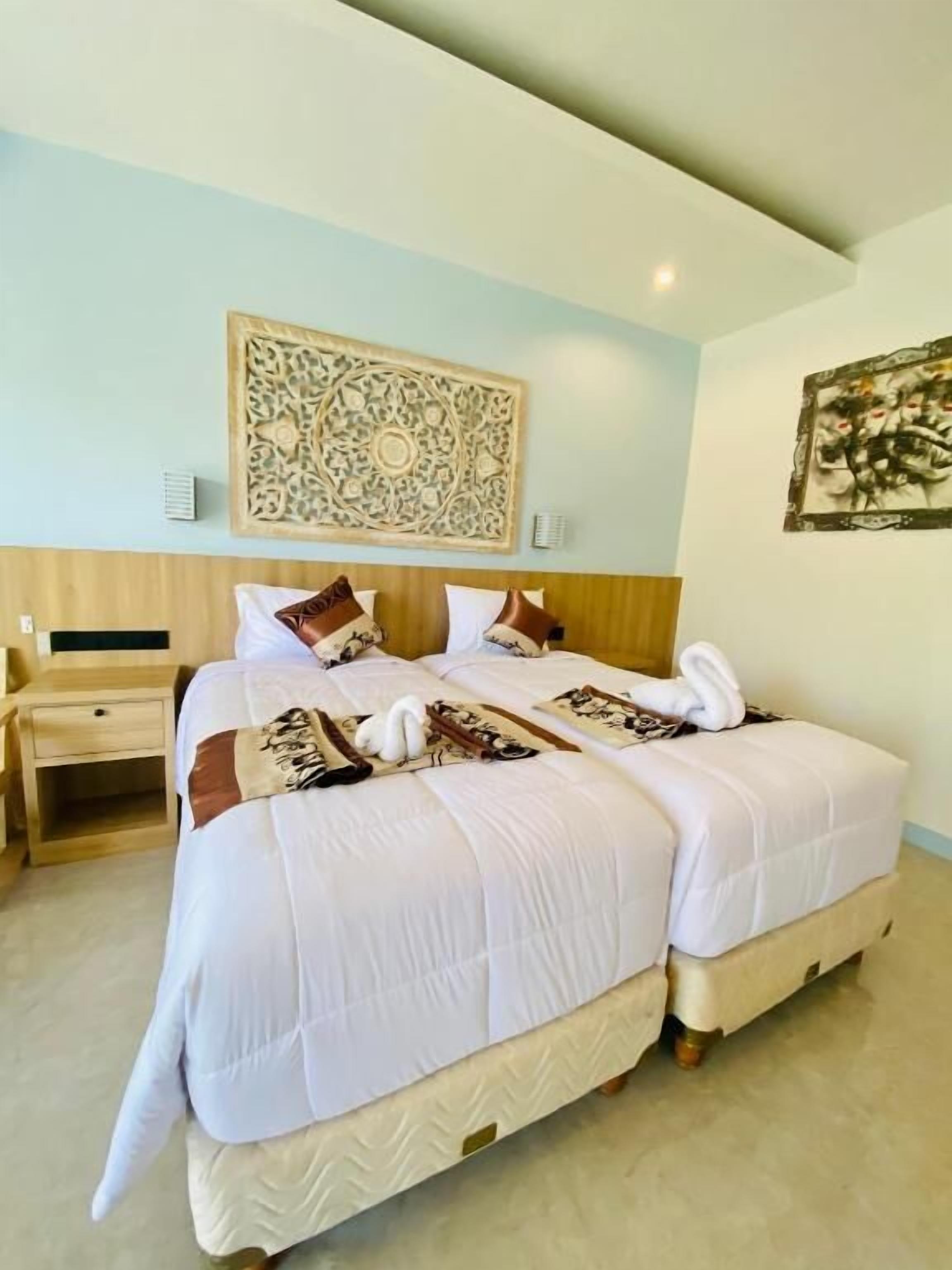 A double bed with white bedding, a wooden headboard, a nightstand, and a decorative wall piece.