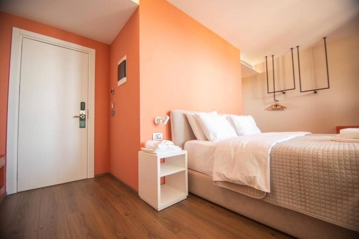 Un dormitorio con una cama, una mesita de noche, una puerta y una lámpara fijada a la pared.