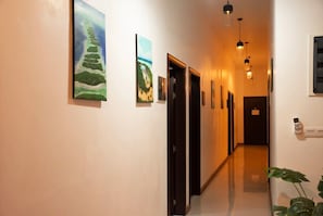 A hallway with artwork on the walls, a plant on the right, and a door at the end.