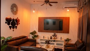 Una sala de estar con una televisión de pantalla plana montada en un panel de madera, sofás de cuero, una mesa de centro y un ventilador de techo.