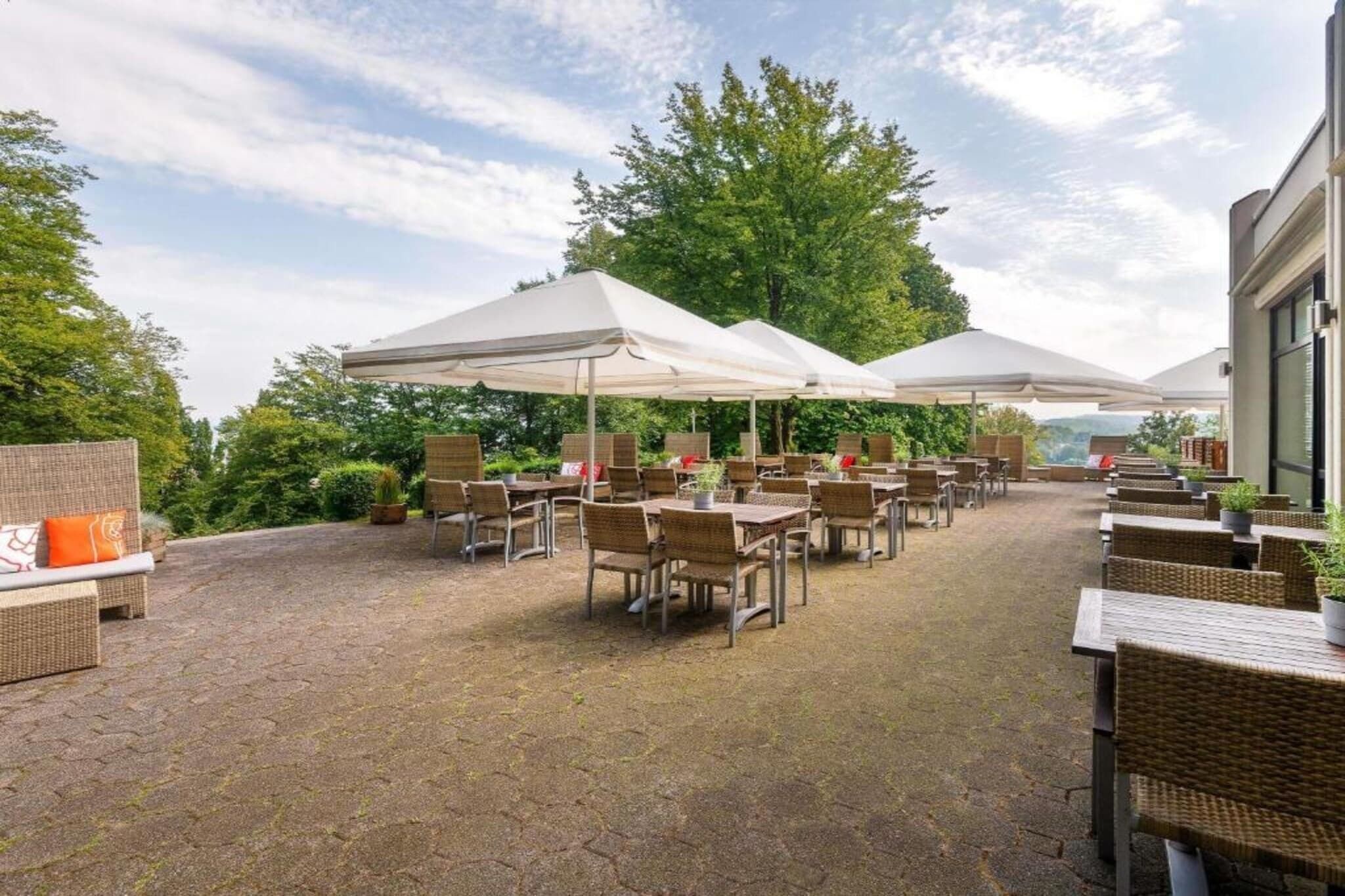 Ein Terrassenbereich im Freien mit Korbmöbeln und weißen Sonnenschirmen.