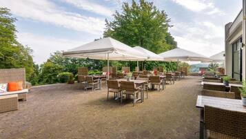 Ein Terrassenbereich im Freien mit Korbmöbeln und weißen Sonnenschirmen.