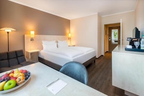 A hotel room with a bed, bedside tables, a desk with a fruit bowl, and a sofa.