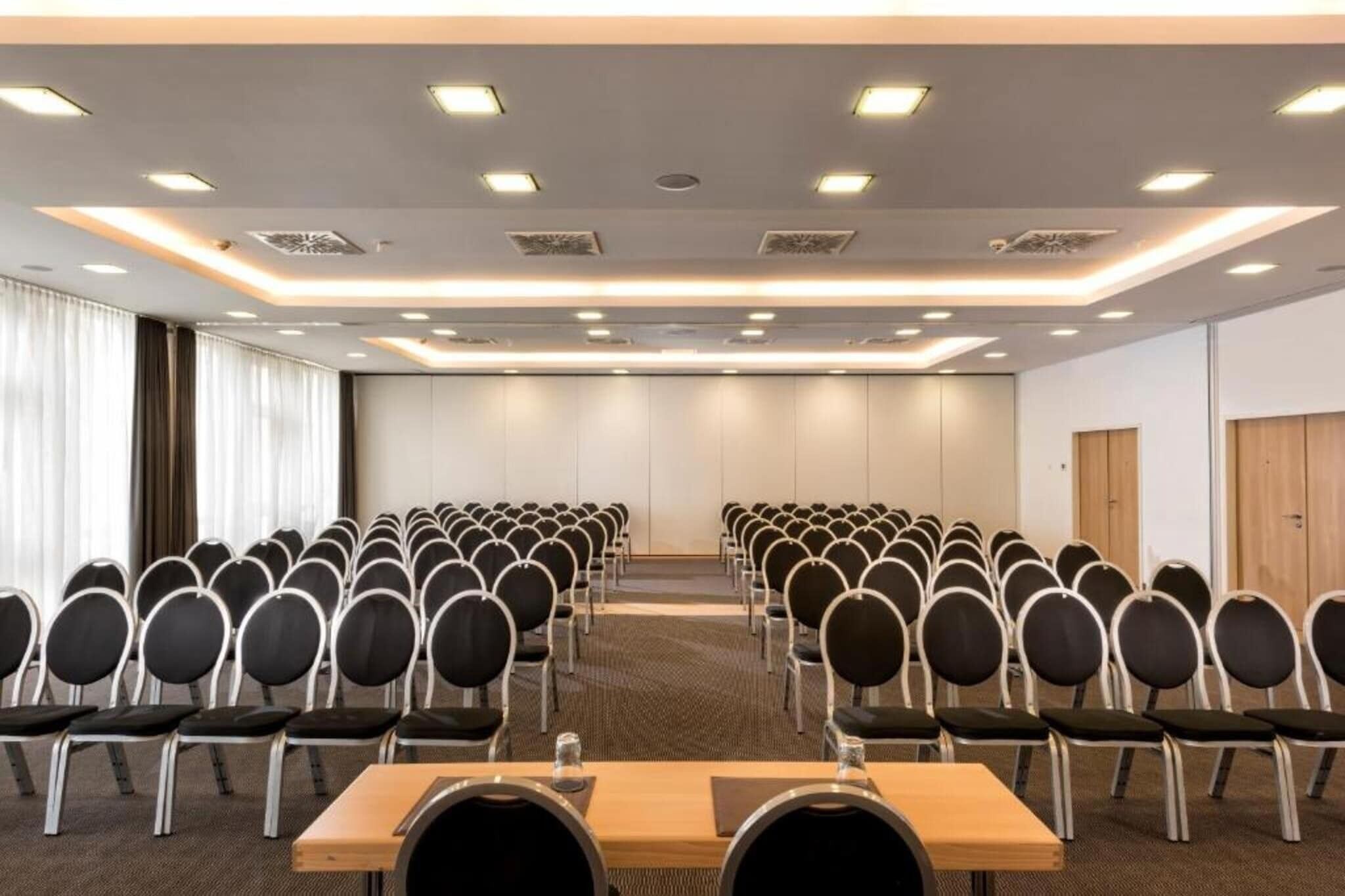 A conference room with rows of chairs and tables, equipped with ceiling lights and ventilation.