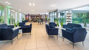 A modern hotel lobby with dark blue armchairs, a reception desk, and large windows offering a view of greenery.
