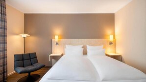 A hotel room with a large bed, two bedside tables, a modern chair, and wall-mounted lamps.