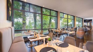 A modern restaurant with large windows, wooden tables, and comfortable seating.