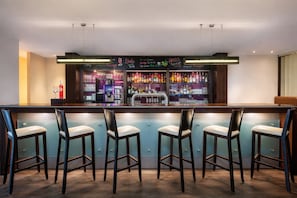A bar area with a counter, bar stools, and shelves of liquor bottles.