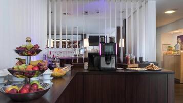 Ein Bereich mit Buffet, einer Kaffeemaschine, Obstschalen und einer Bar im Hintergrund.