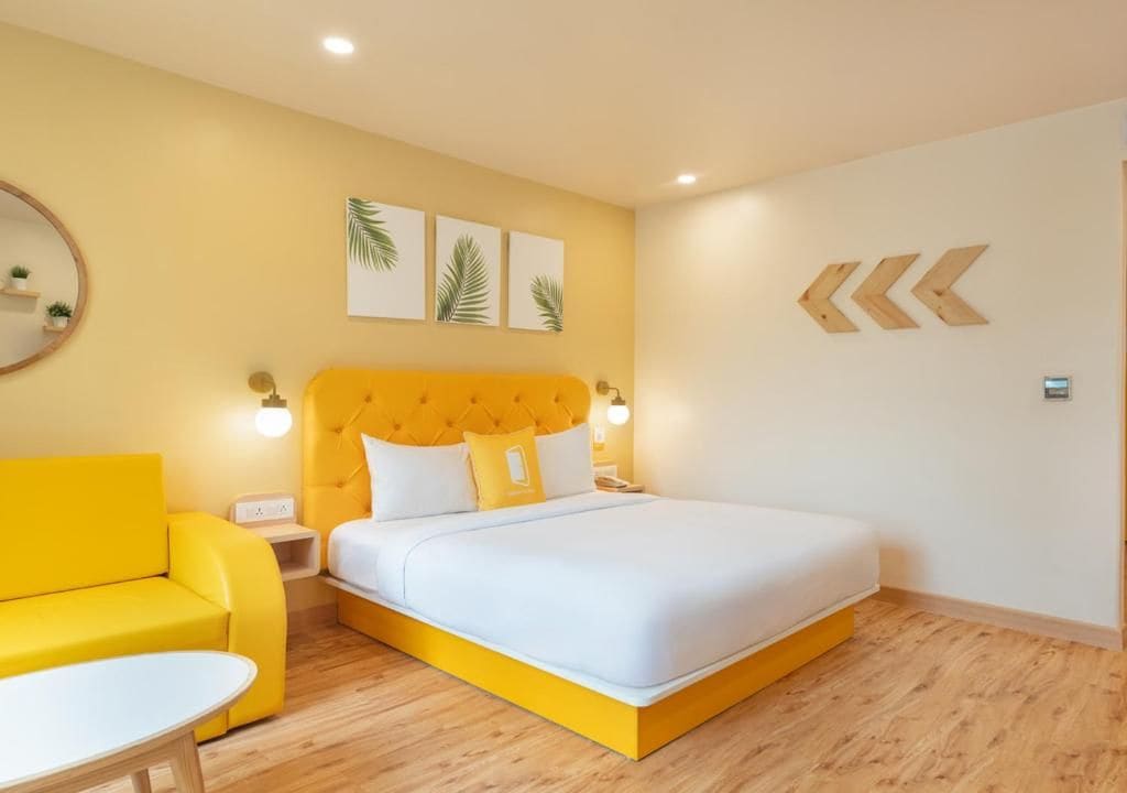 Ein Zimmer mit einem Bett, einem gelben Sofa, einem runden Tisch und Wandbildern.