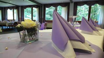 Ein Hotelzimmer mit großem Fenster, einem Tisch mit Blumenvase und einer violetten Tischdecke.