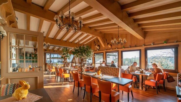 Un restaurant avec des poutres en bois, des chaises orange et de grandes fenêtres.