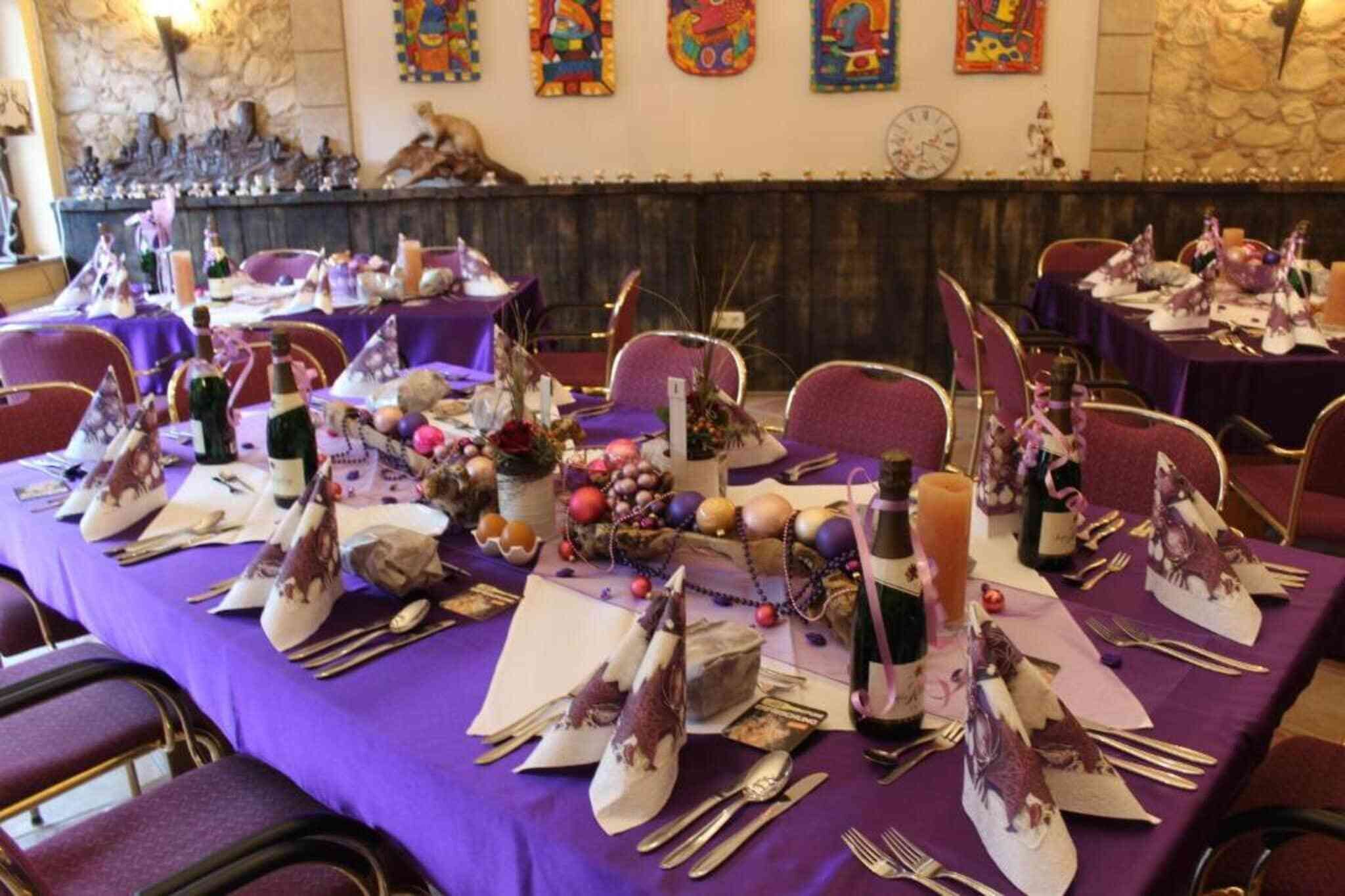 En festlokal med bord uppdukade för ett formellt evenemang, med lila dukar och dekorativa bordsdekorationer.