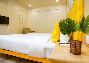 A hotel room with a bed, a bedside table, a TV, and a plant. - Bloom Hotel - Koregaon Park (PUNE)