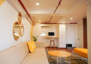 A modern room with a sofa, a round table, a desk with a computer, and a mirror on the wall. - Bloom Hotel - Koregaon Park (PUNE)