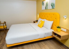 Una cama con cabecera amarilla, ropa de cama blanca y una pequeña planta amarilla sobre una mesita de noche.