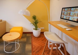 A modern office space with a desk, computer, chair, lamp, and a potted plant. - Bloom Hotel - Koregaon Park (PUNE)