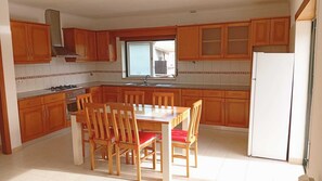 A kitchen with wooden cabinets, a gas stove, a sink, and a dining table with chairs. - Junqueira Eden 
Private 2-Bedroom House with Balcony, BBQ & Shared Pool (Alcobaça)