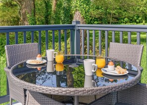 A round table with wicker chairs, breakfast items, and a glass of orange juice on a balcony with a blue railing and greenery in the background. - Luxury 2 Bedroom Hot Tub sleeps 6 (Hayle)