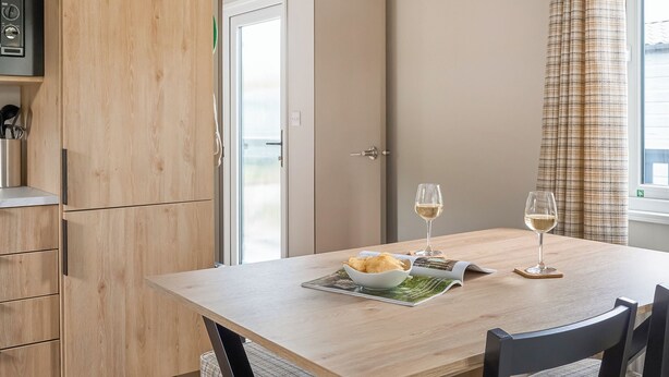 Een eethoek met een tafel, stoelen, een schaal chips en twee glazen witte wijn.