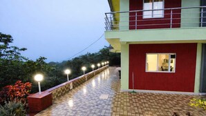 A two-story building with a red and green exterior, a balcony, and a tiled walkway. - Red Soil Strawberry Farm villa (Bhuteghar)