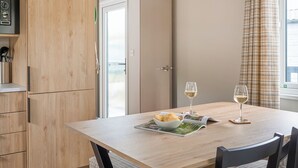 Uma área de refeições com uma mesa, cadeiras, uma tigela de batatas fritas e duas taças de vinho branco.