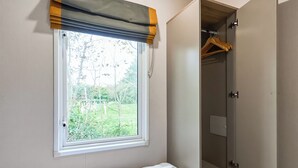 Quarto com janela, cama e guarda-roupa com toalha branca.