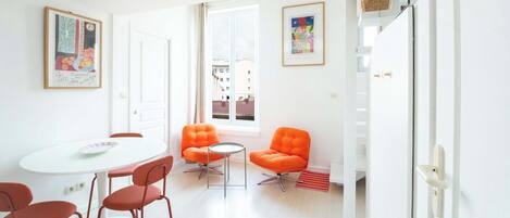 A bright, modern room with a white table, orange chairs, and two framed artworks on the walls.