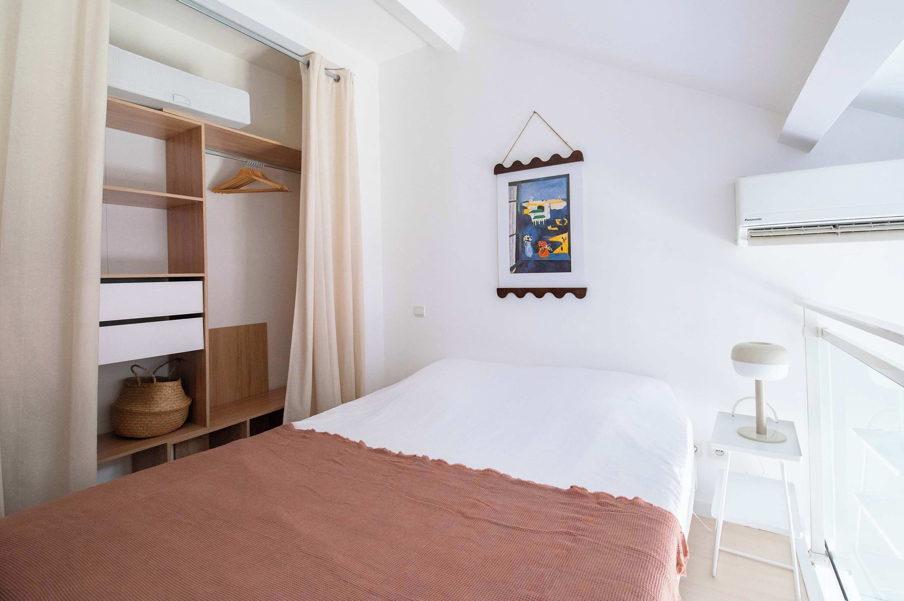 A bedroom with a bed, a wardrobe, a bedside table, and a wall-mounted air conditioner.