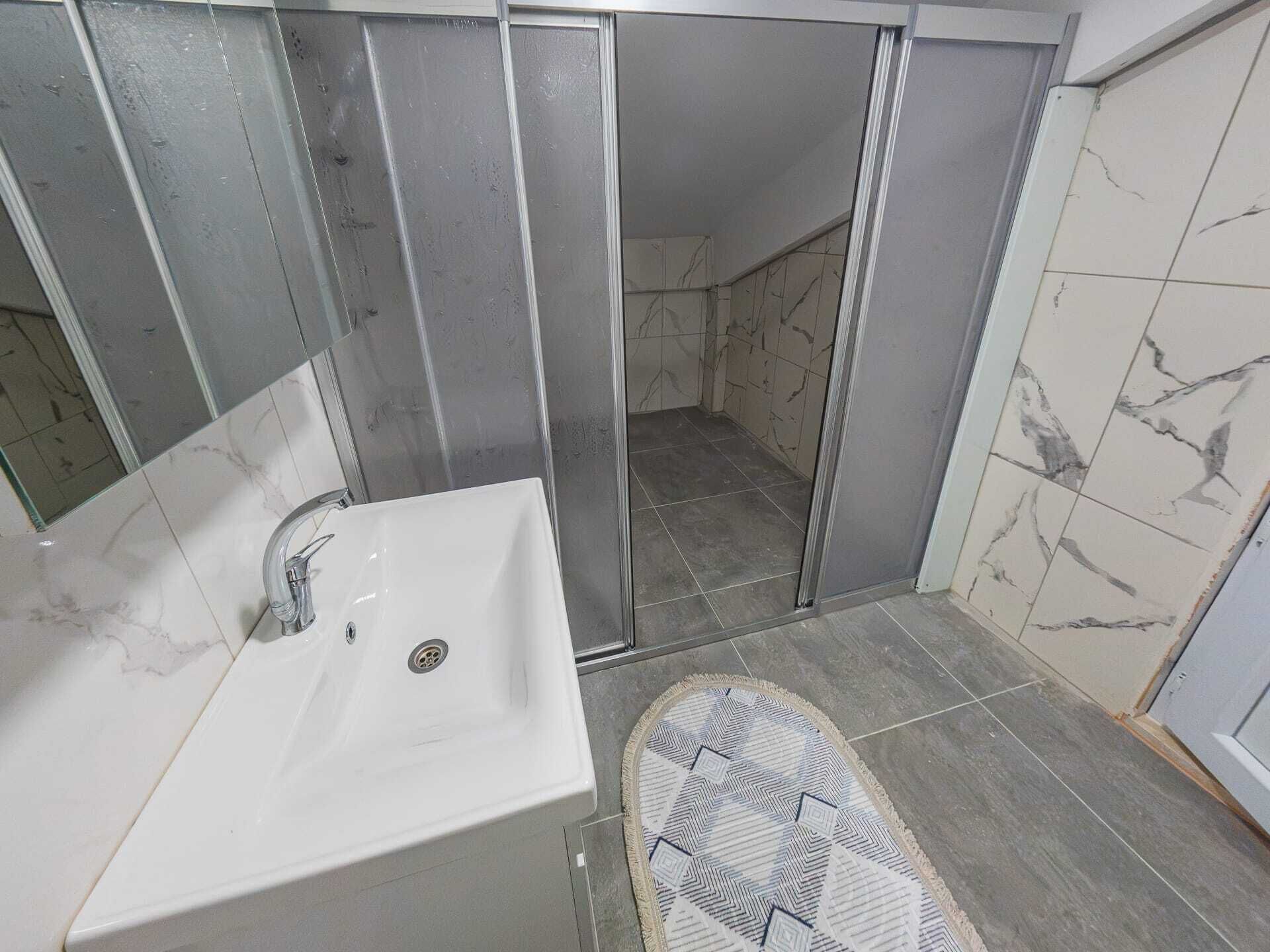 Un baño con lavamanos blanco, cabina de ducha y alfombra estampada.