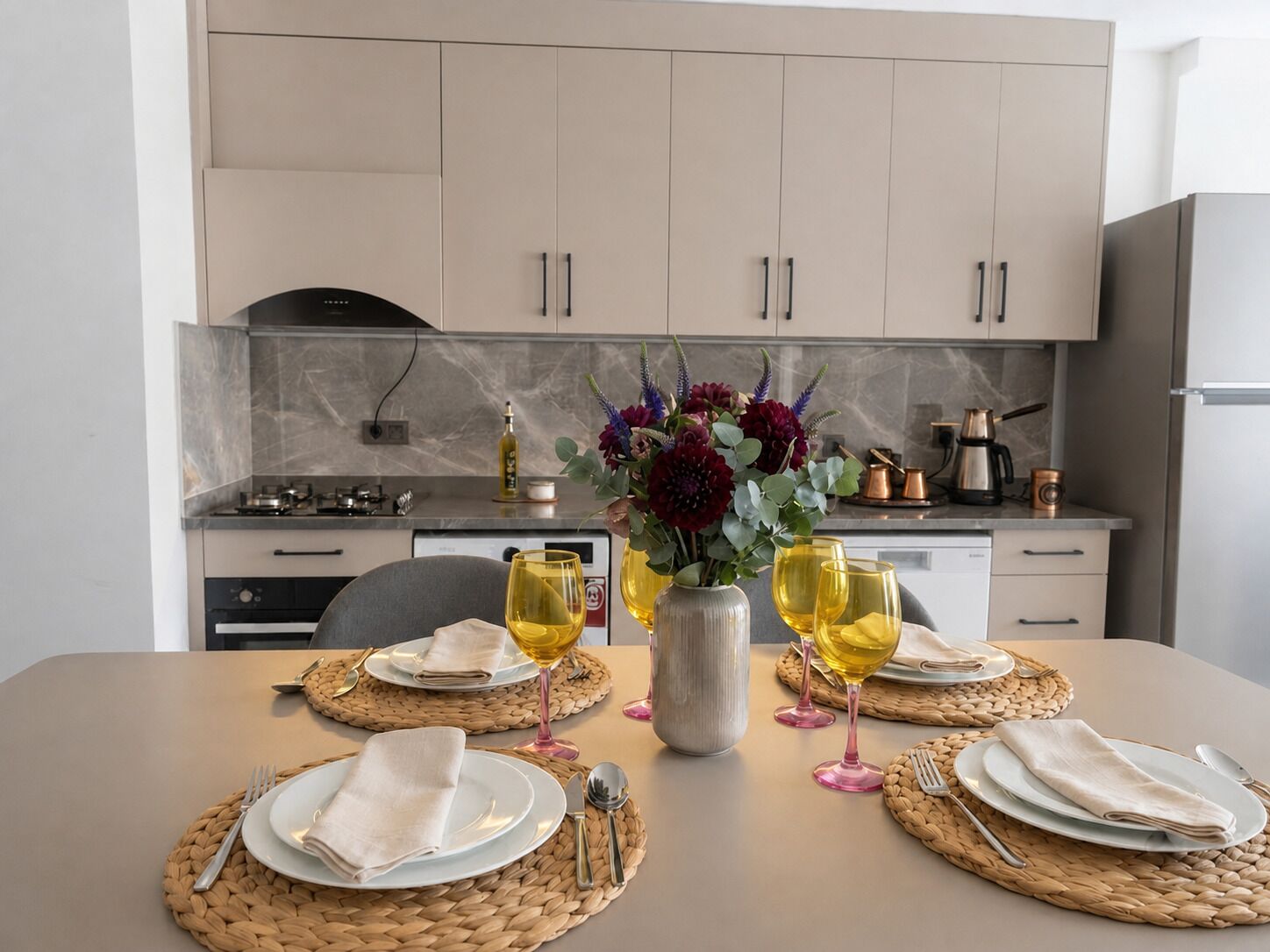 Una mesa de comedor dispuesta con platos, cubiertos y copas de vino, con un jarrón de flores en el centro.