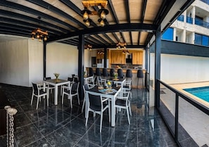A rooftop dining area with tables and chairs, a pool, and a view of the building's interior.