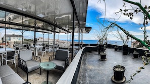 A rooftop terrace with outdoor seating, potted plants, and a view of the sea.