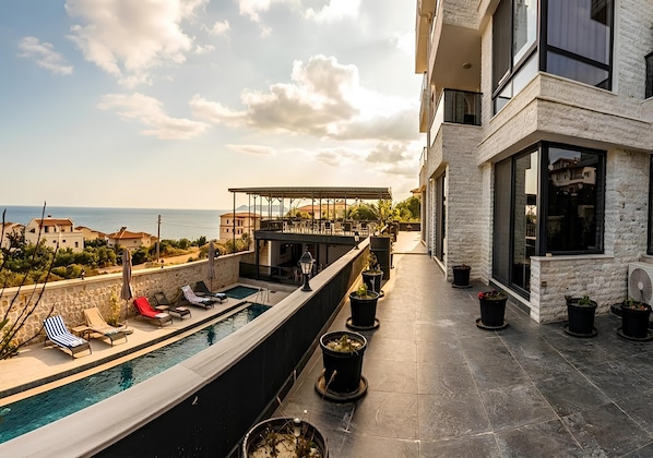 A rooftop pool area with lounge chairs, a covered seating area, and potted plants.