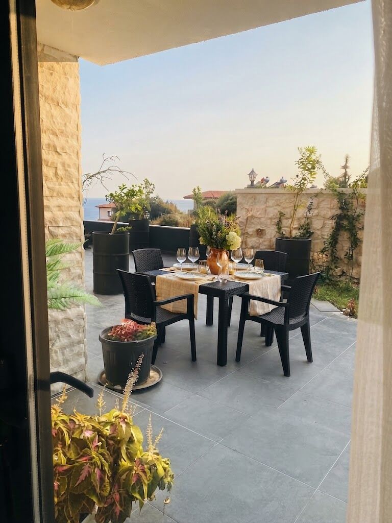 An outdoor dining area with a table set for two, surrounded by chairs, and a view of the sea in the background.