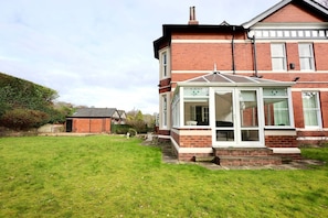 A two-story house with a conservatory, a brick exterior, and a well-maintained lawn. - Somerley Halifax - Luxury 6 Bedroom Stay (West Yorkshire)