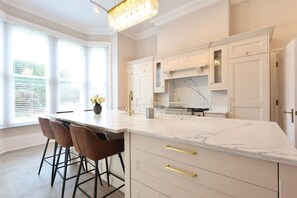 Une cuisine moderne avec un plan de travail en marbre, des tabourets de bar et un lustre.