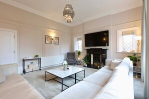 A modern living room with a fireplace, a large TV, and a comfortable seating area. - Somerley Halifax - Luxury 6 Bedroom Stay (West Yorkshire)