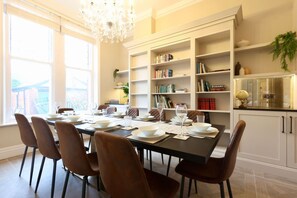 Une salle à manger avec une table noire dressée pour six personnes, entourée de chaises marron, et une bibliothèque remplie de livres et d’objets décoratifs placée sur le côté.