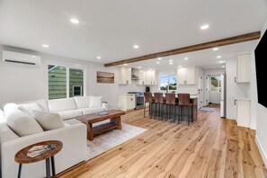 A modern kitchen with white cabinets, a central island with bar stools, and a dining area with a white sofa and coffee table. - Sunny 3BR Retreat Near Everett Waterfront (Everett)